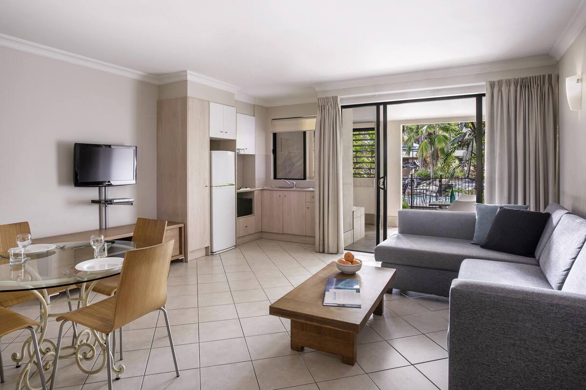 A modern hotel room with a dining area, a sofa, a TV, and a balcony with a view.