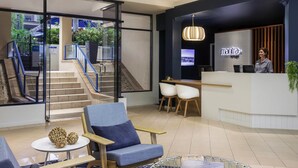 A hotel lobby with a reception desk, seating area, staircase, and large windows offering views of greenery. - Mantra Heritage (Port Douglas)