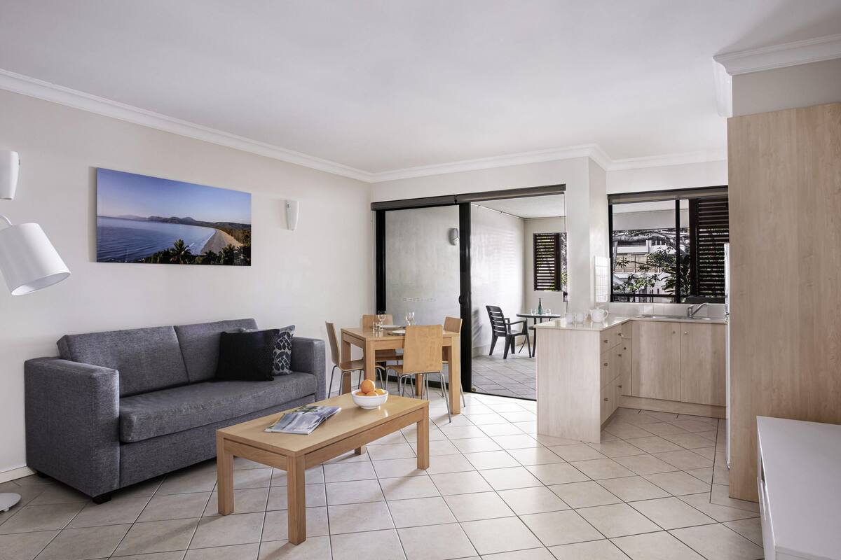A modern living room with a grey sofa, wooden coffee table, and a dining area with a table and chairs.