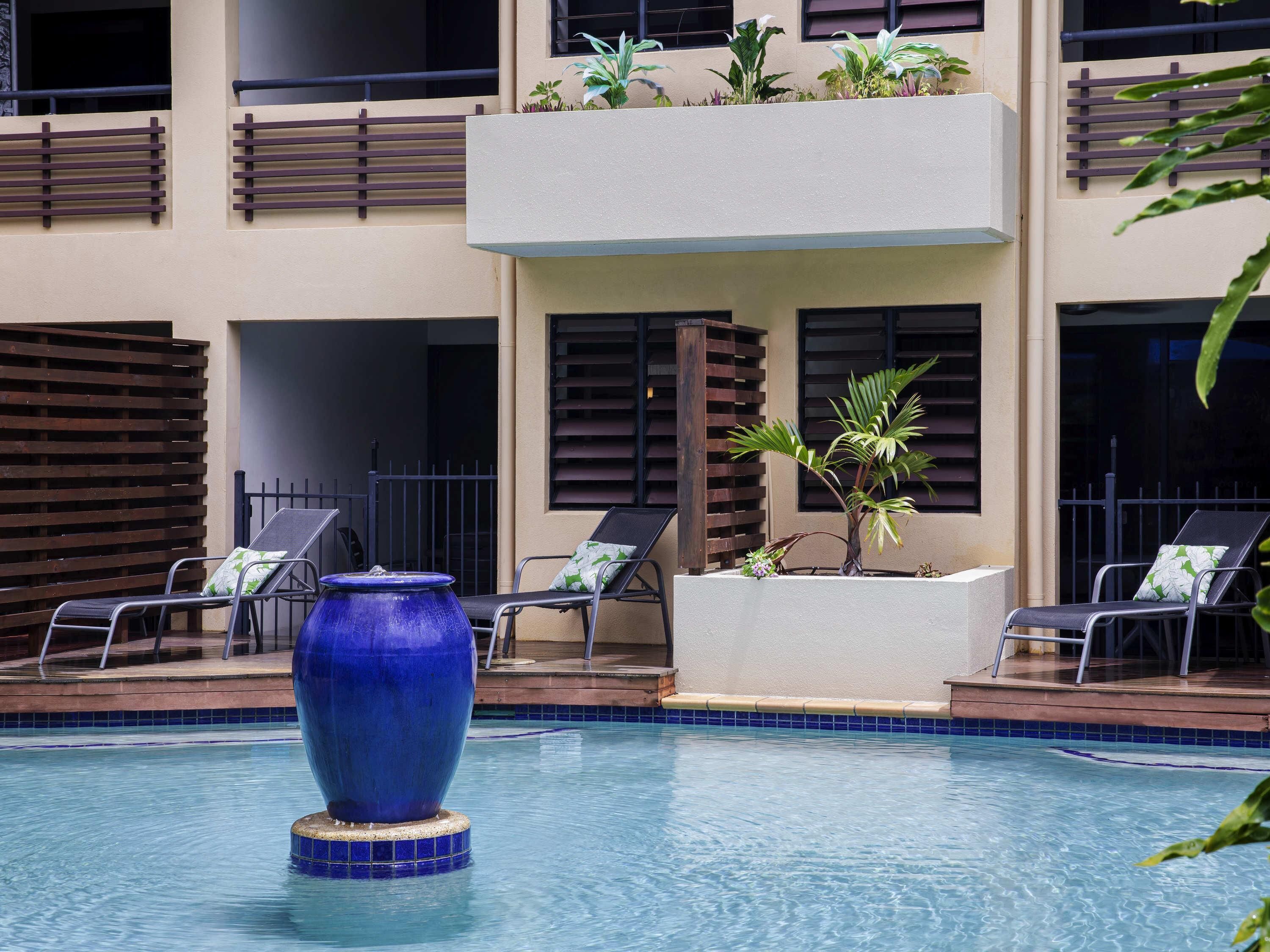 Un espace piscine avec des chaises longues, un vase décoratif bleu et des plantes en pot.