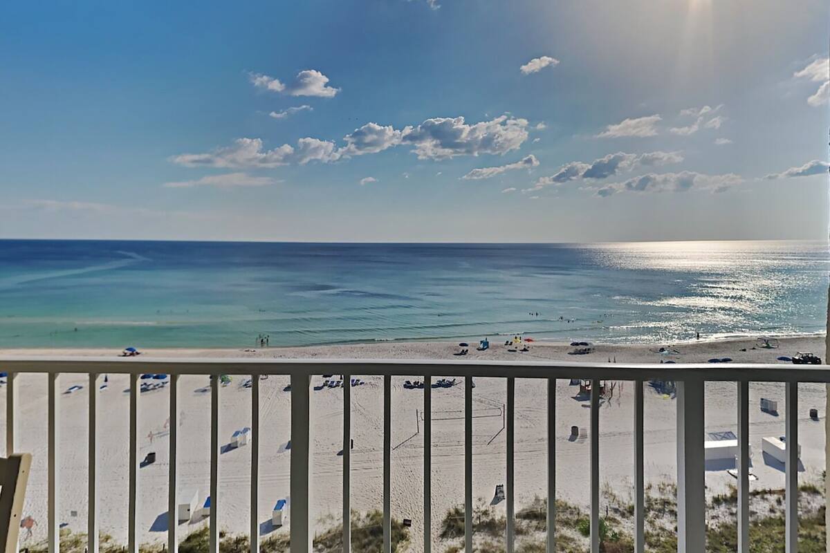 A beach view with a clear sky, calm sea, and a sandy shore with umbrellas and beach chairs.