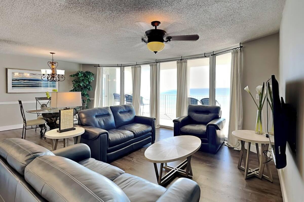 A spacious living room with a large leather sofa, a coffee table, and a ceiling fan.