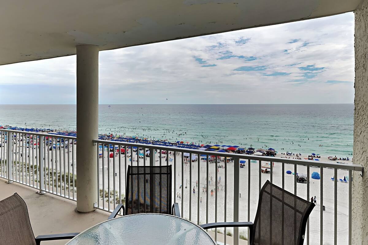 A balcony with a view of a crowded beach and the ocean.