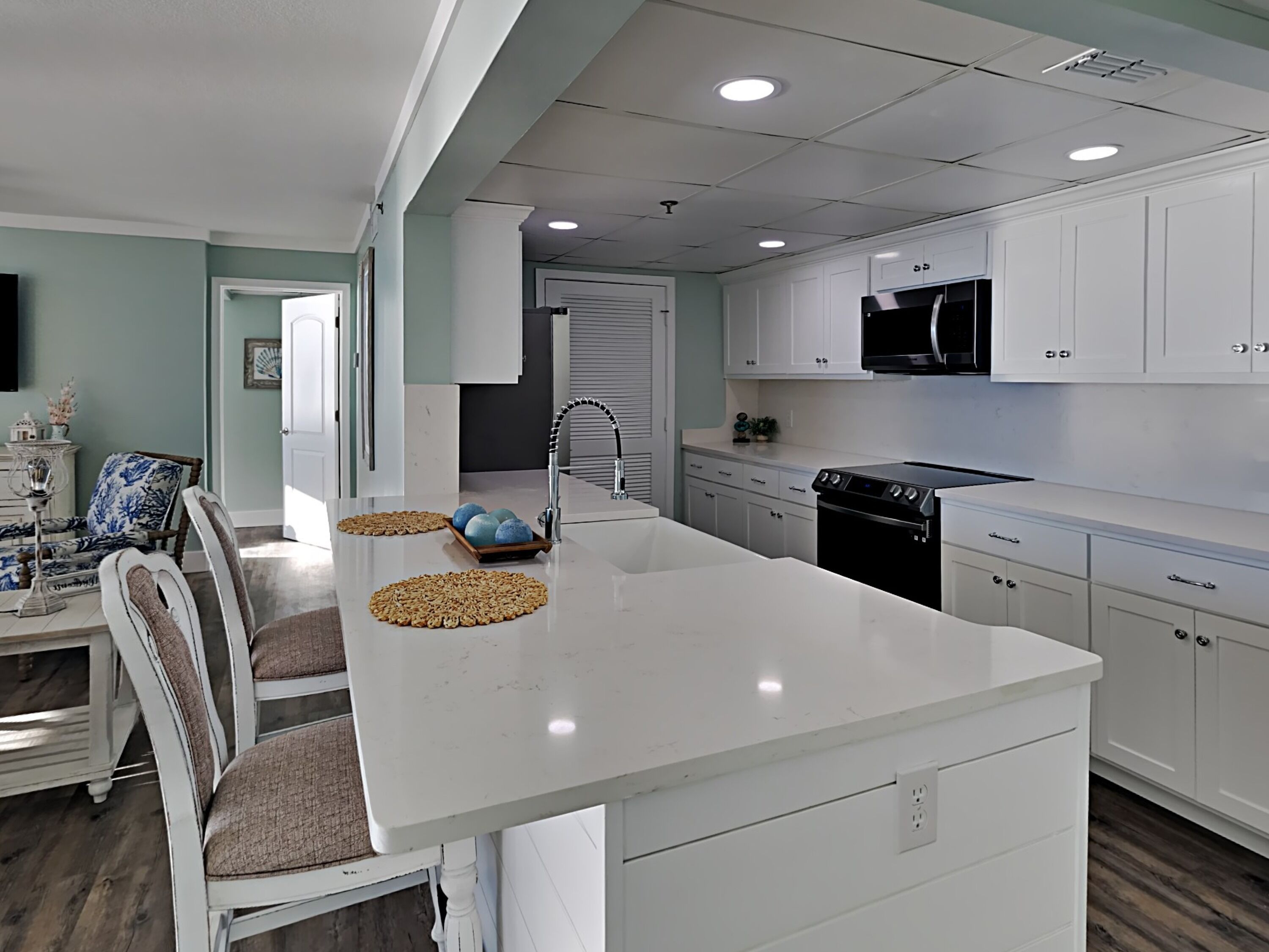 A modern kitchen with white cabinets, a black stove, and a large island with a sink.
