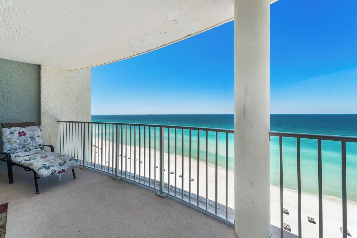 A balcony with a view of the ocean, a chair, and a railing.