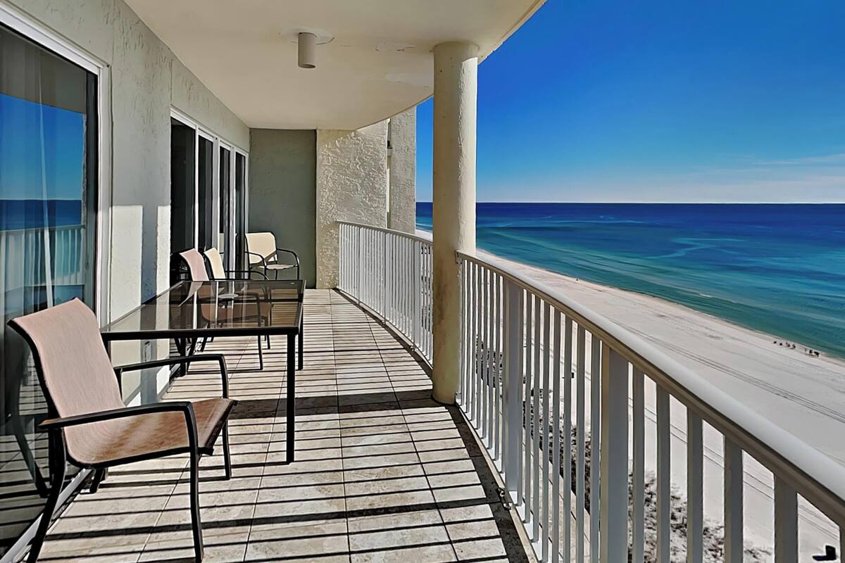 A balcony with a view of the ocean, a table with chairs, and a railing.
