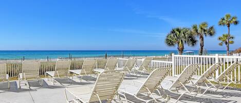 Zona relax in spiaggia con sedie in metallo bianco e una recinzione bianca, con vista sull'oceano.