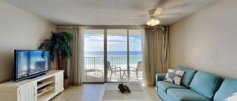 A living room with a television, a sofa, a coffee table, and a view of the ocean through large sliding doors.