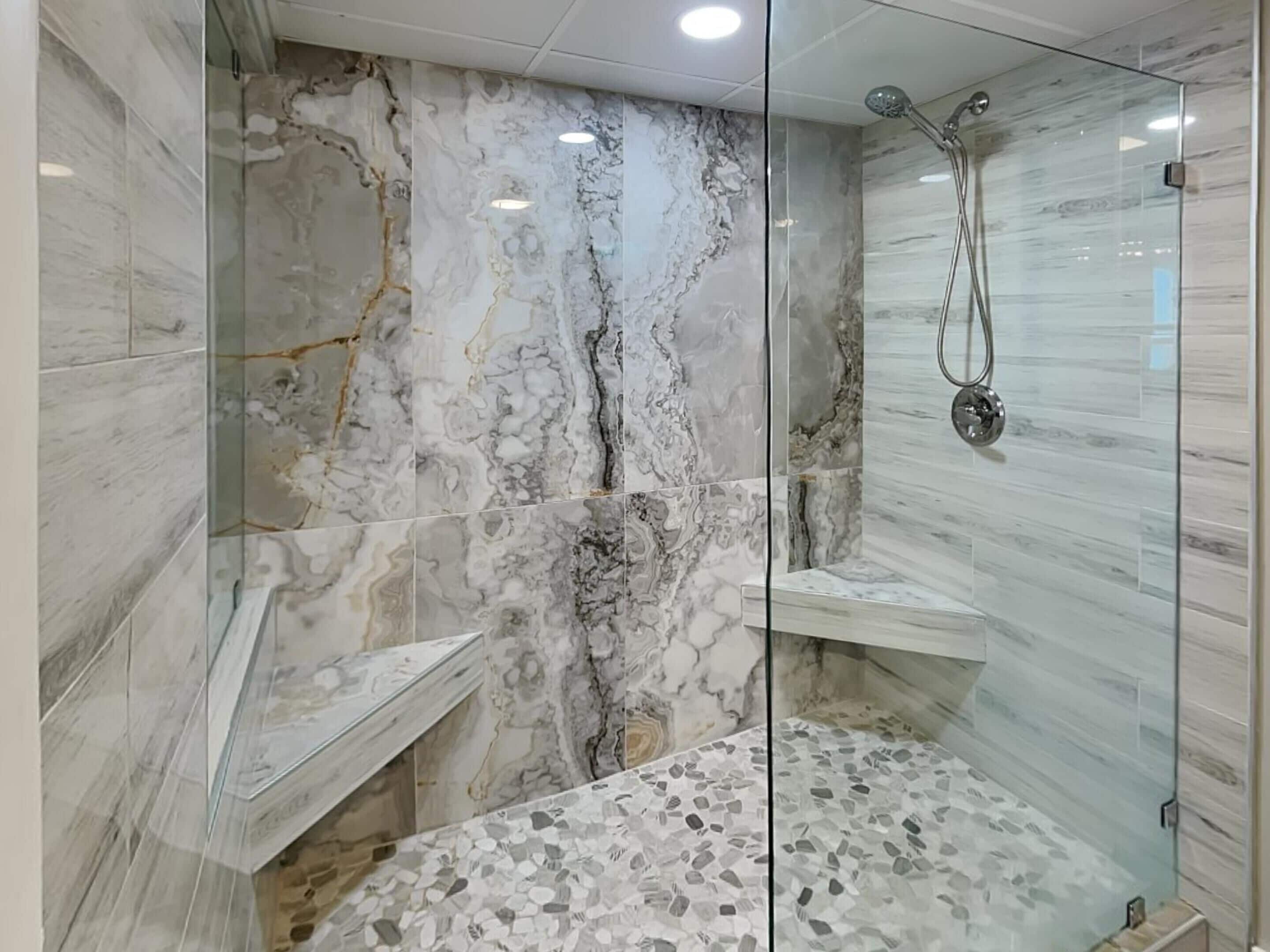 A modern bathroom with marble walls, a glass shower enclosure, and a mosaic floor.