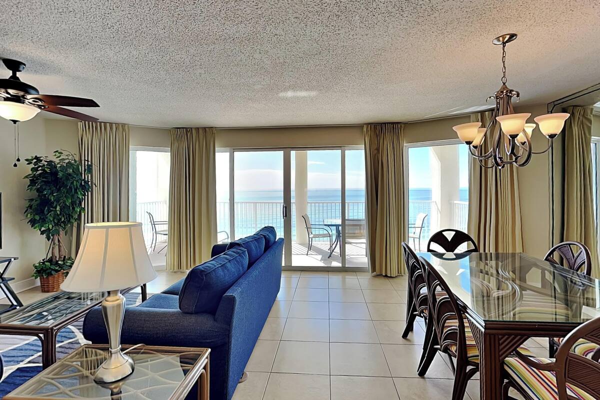 A spacious living area with a sofa, a glass dining table, and a view of the ocean through large sliding doors.