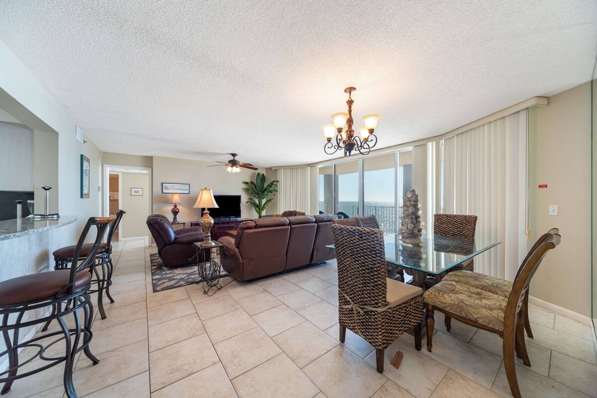 A spacious living room with a glass coffee table, leather sofa, and a dining area with a glass top table and chairs.