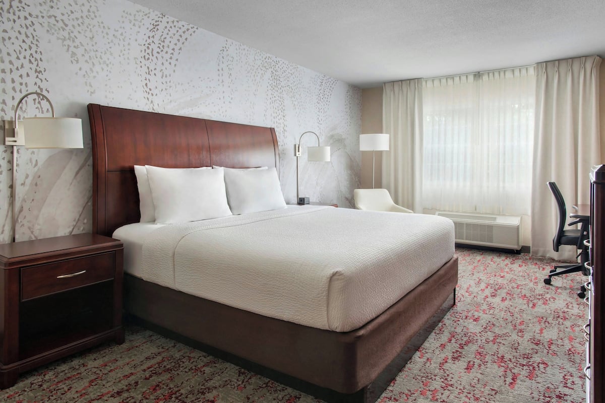 Una habitación de hotel con una cama grande, mesitas de noche, un escritorio y una silla.