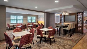 A hotel lobby with multiple seating areas, including tables and chairs, a large flat-screen TV mounted on the wall, and a patterned carpet. - Fairfield Inn & Suites by Marriott Great Barrington Lenox/Berkshires (Great Barrington)