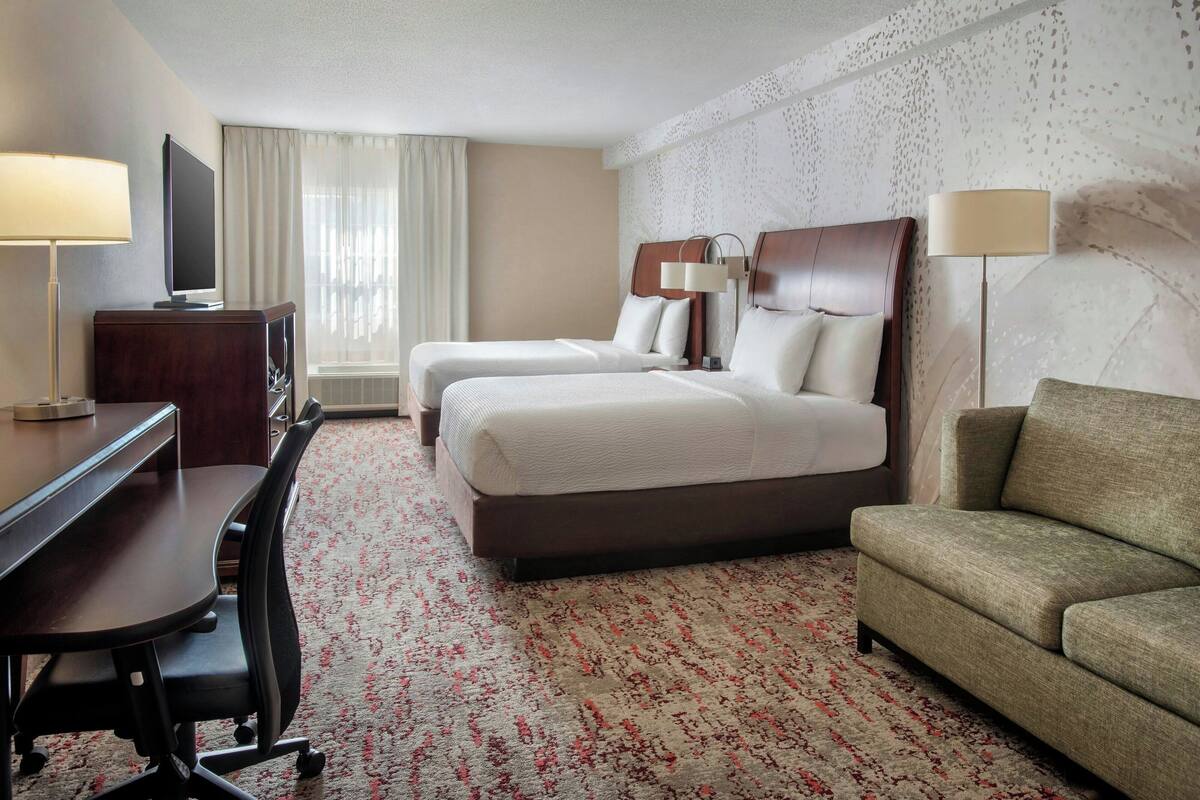 Una habitación de hotel con dos camas, un escritorio, una silla, un sofá y una televisión.