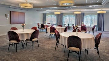 Un salón de conferencias con mesas y sillas redondas, ventanas amplias con cortinas y un diseño de techo moderno.