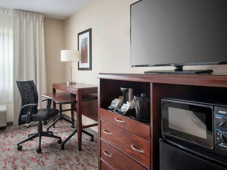 A hotel room with a desk, chair, television, microwave, and a framed picture on the wall.