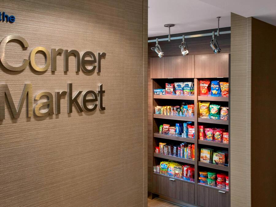 Een buurtwinkel met een bord waarop 'the Corner Market' staat, en schappen vol met verschillende snacks en levensmiddelen.
