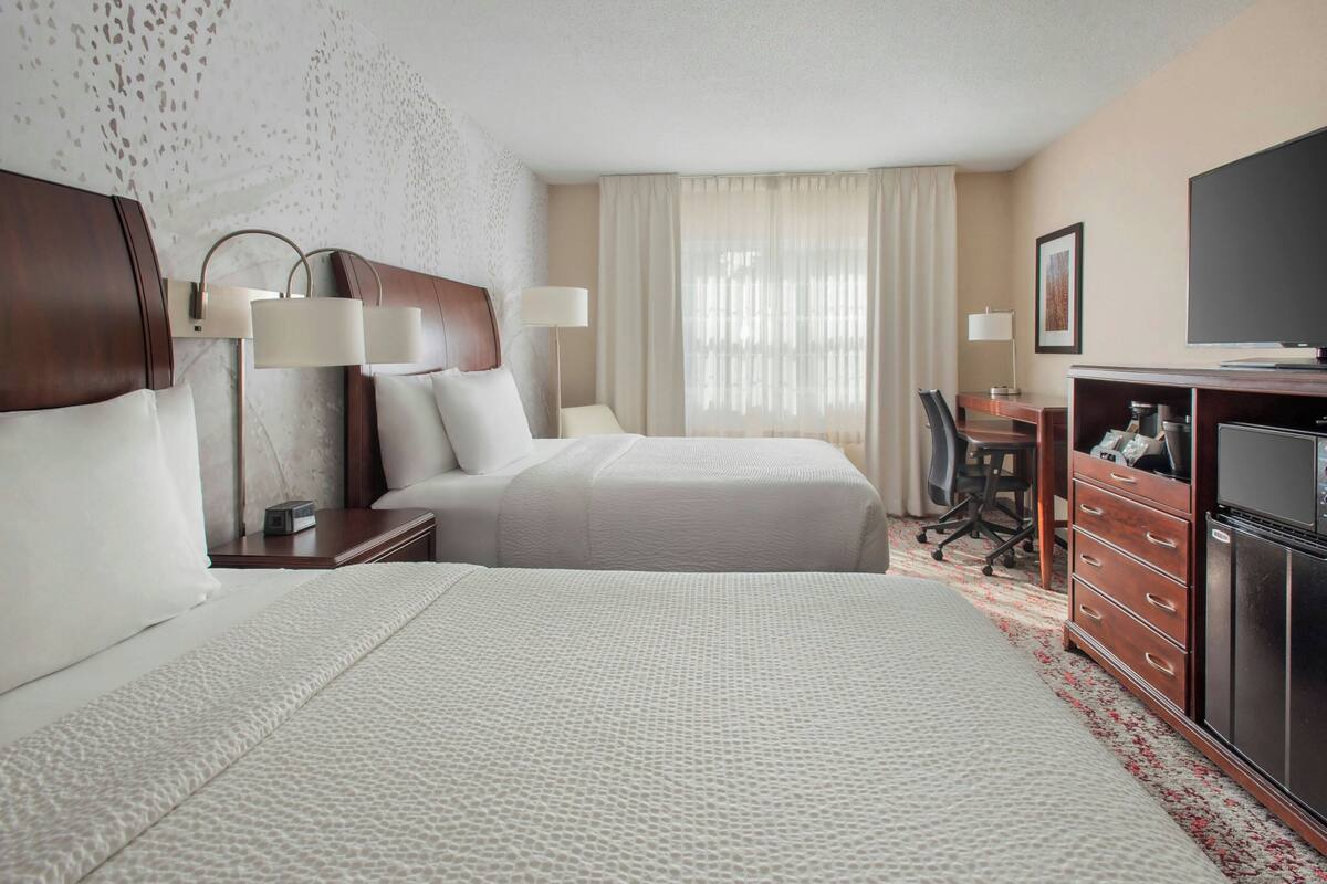 Una habitación de hotel con dos camas, un escritorio, un televisor y un aparador.