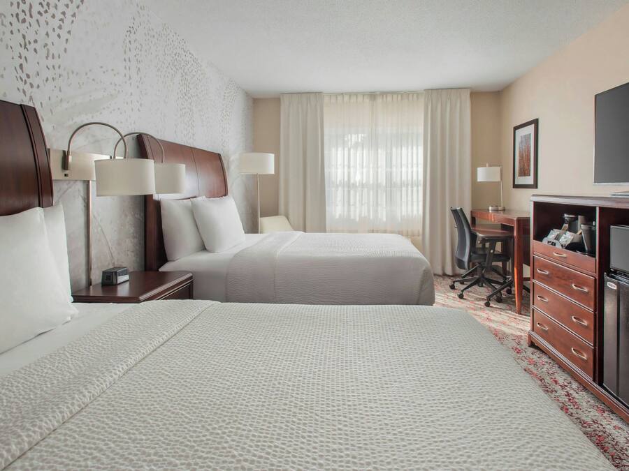 A hotel room with two beds, a desk, a television, and a dresser.