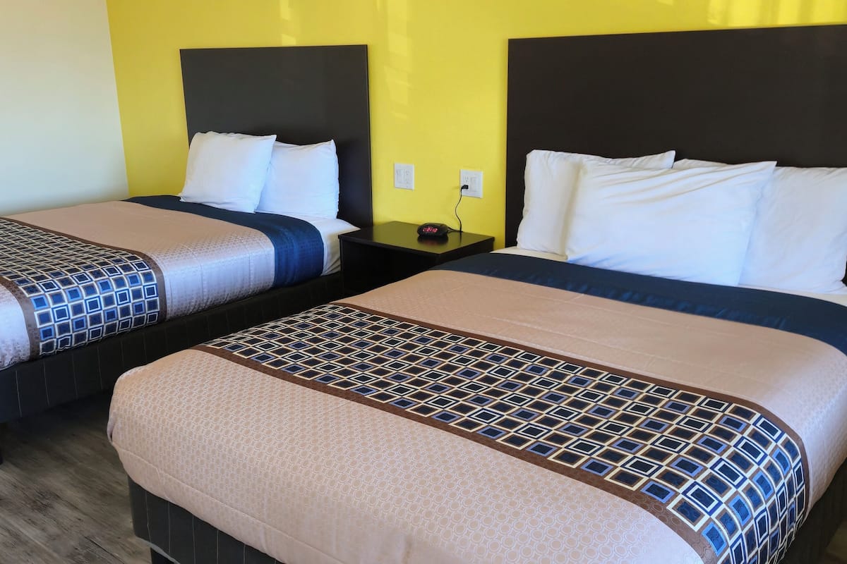 Two single beds with headboards, a nightstand with a lamp, and a yellow wall.