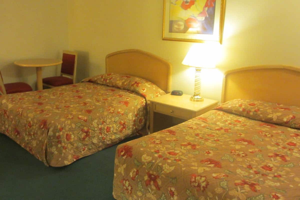 A hotel room with two beds, a small table, a chair, and a lamp.