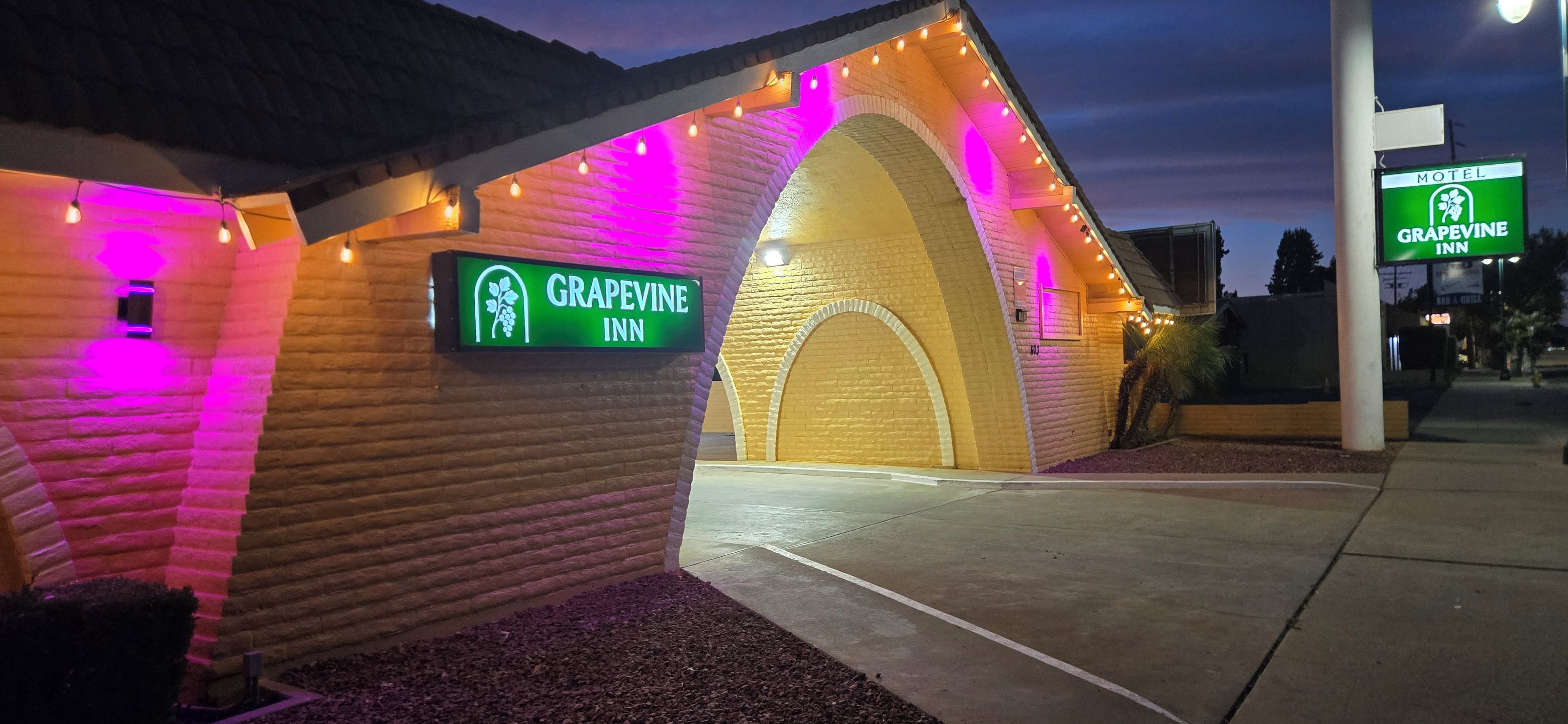 A brick building with a sign for Grapevine Inn, featuring an arched entrance and string lights.