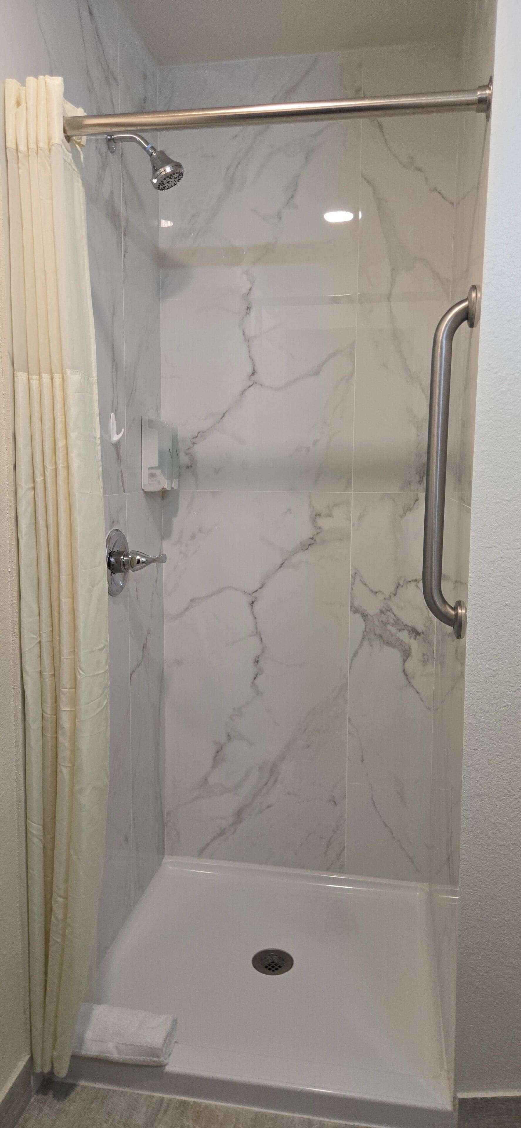 A walk-in shower with a glass door, a showerhead, and a handrail.