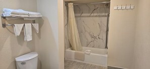 A bathroom with a toilet, a towel rack with folded towels, a shower with a marble wall, and a bathtub.