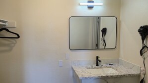 A bathroom with a white sink, a mirror, a hairdryer, and a black hanger on a white wall. - Grapevine Inn (Lodi)