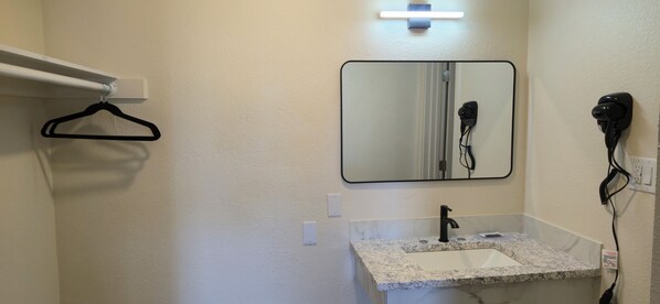 A bathroom with a white sink, a mirror, a hairdryer, and a black hanger on a white wall. - Grapevine Inn (Lodi)