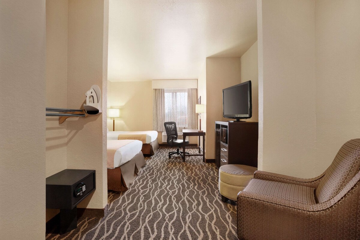 Een hotelkamer met een bed, bureau, stoel, televisie en een minibar.