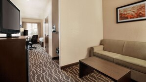 Una habitación de hotel con sofá, mesa de centro, televisor, escritorio y alfombra estampada.