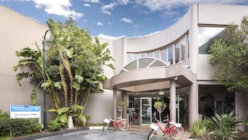 Contemporary building with a curved facade, featuring large windows and a glass entrance, surrounded by lush greenery.