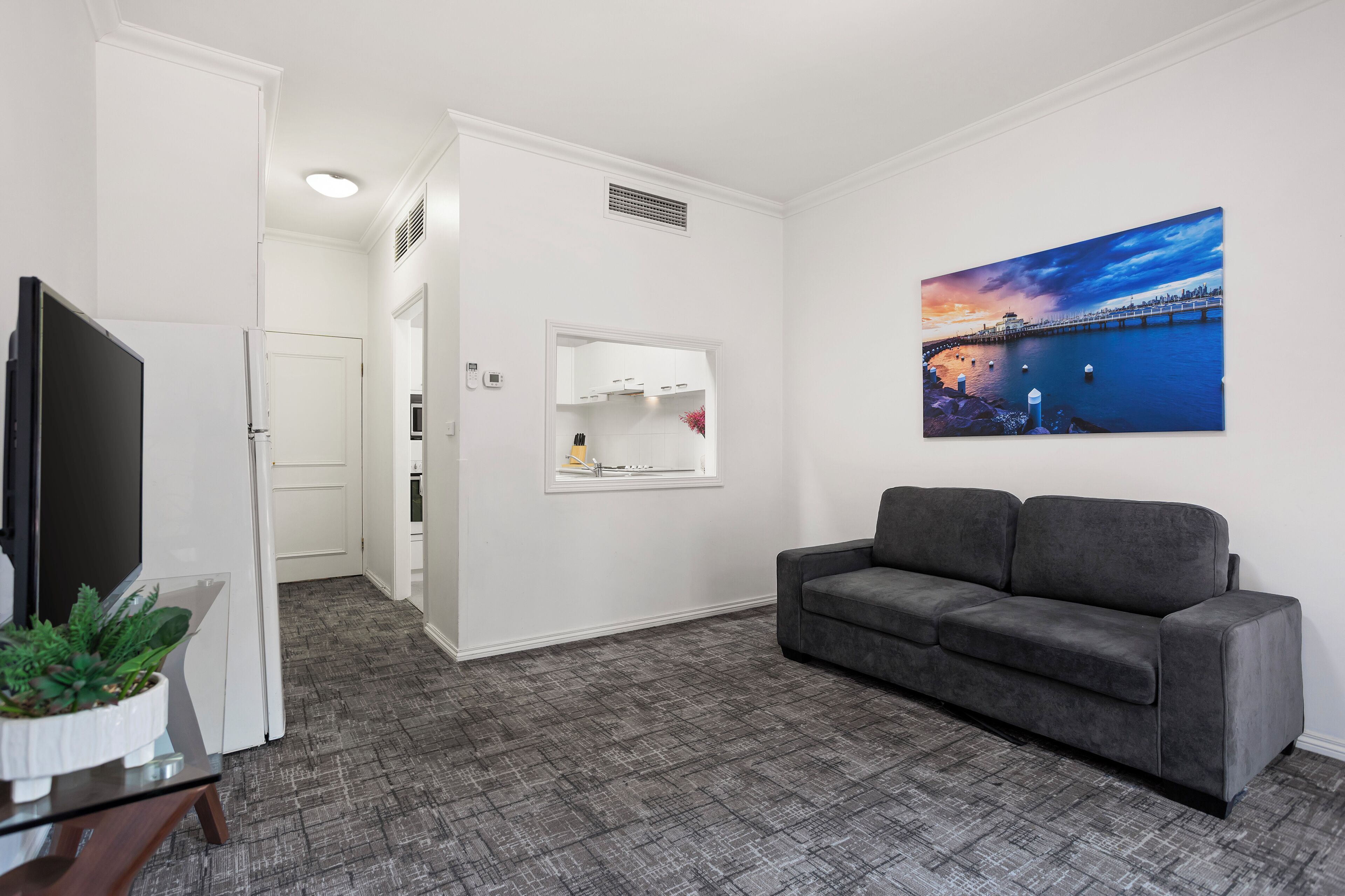 A modern living room with a grey sofa, a flat-screen TV, and a painting of a cityscape.