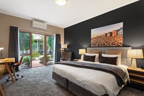 Een hotelkamer met een groot bed, twee nachtkastjes met lampen, een bureau met stoel en uitzicht op de omgeving.
