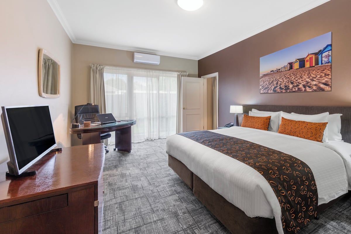 Une chambre d’hôtel équipée d’un lit, d’un bureau, d’une télévision et ornée d’un tableau représentant une scène de plage.
