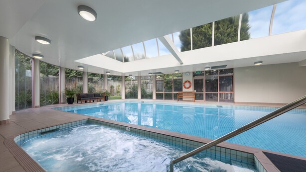 Piscina interior com hidromassagem, cercada por amplas janelas e um banco.