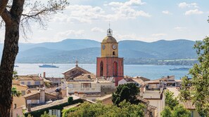 A coastal town with a prominent clock tower, terracotta-roofed buildings, and a body of water with boats. - Hôtel La Tartane Saint -Tropez (Saint-Tropez)