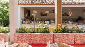 A covered outdoor dining area with red cushioned seating, woven placemats, and a ceiling fan.