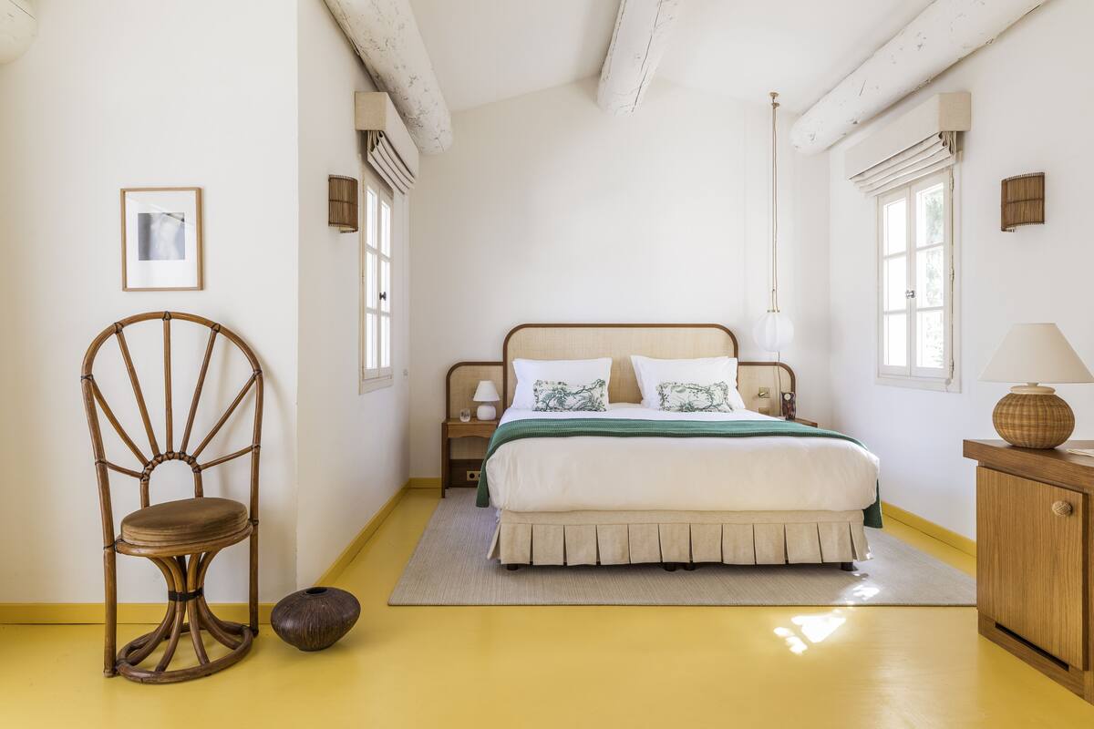 Een slaapkamer met een bed, een stoel, een nachtkastje, een lamp en een raam.