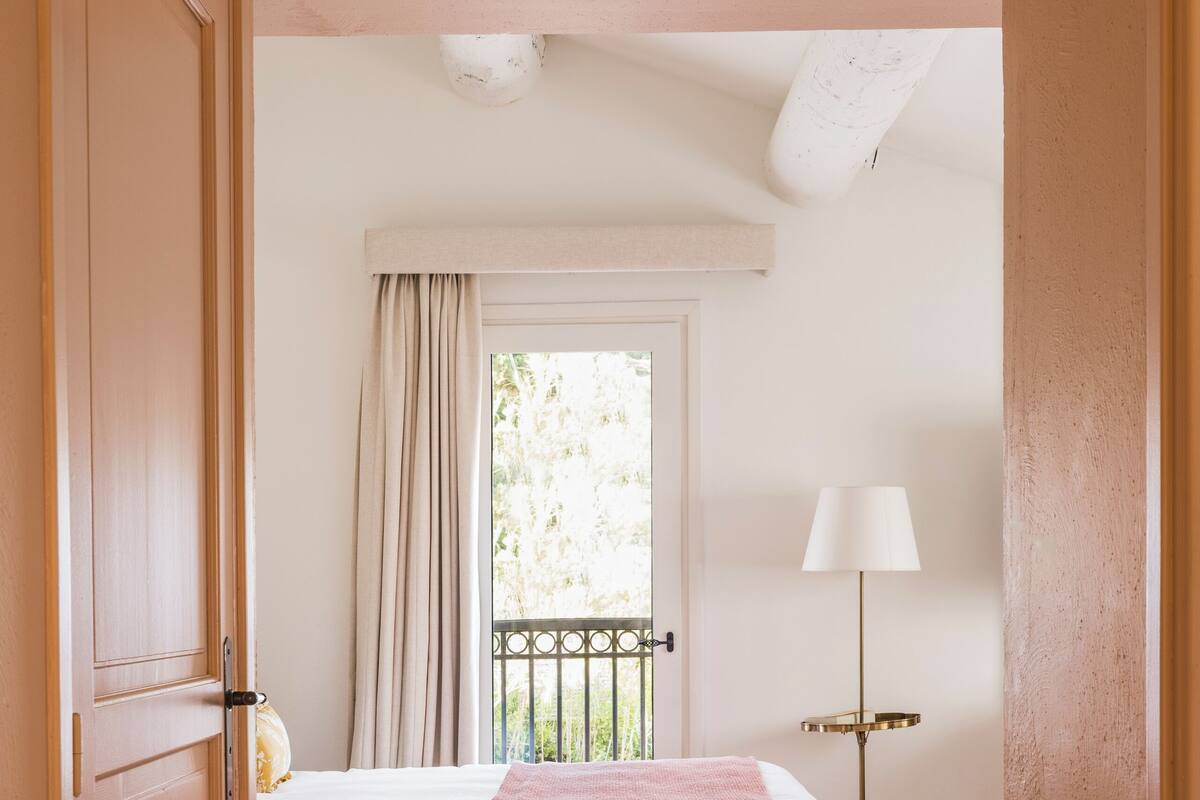 Een slaapkamer met een bed, een raam met gordijnen, een lamp en een deur.
