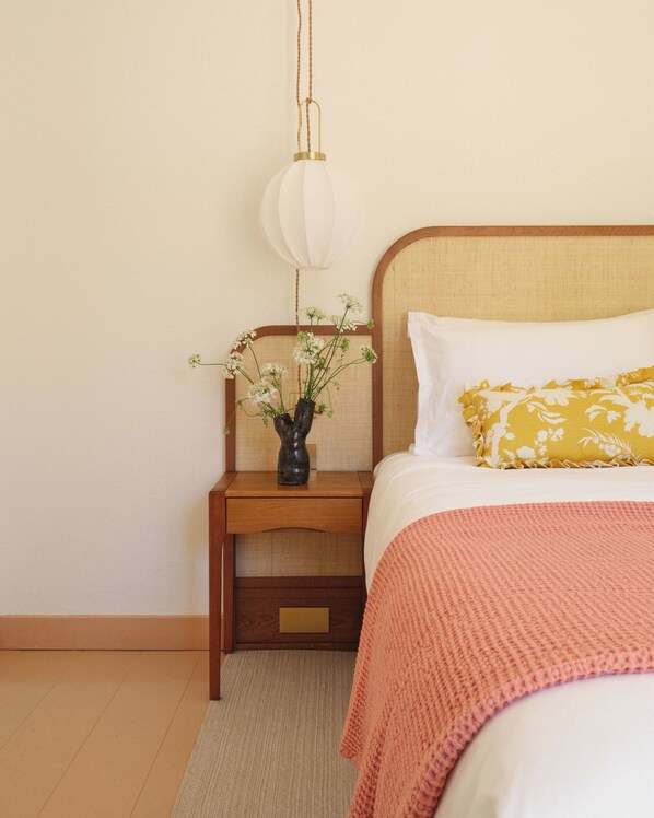 Un dormitorio con cama, mesita de noche, lámpara y un florero con flores.