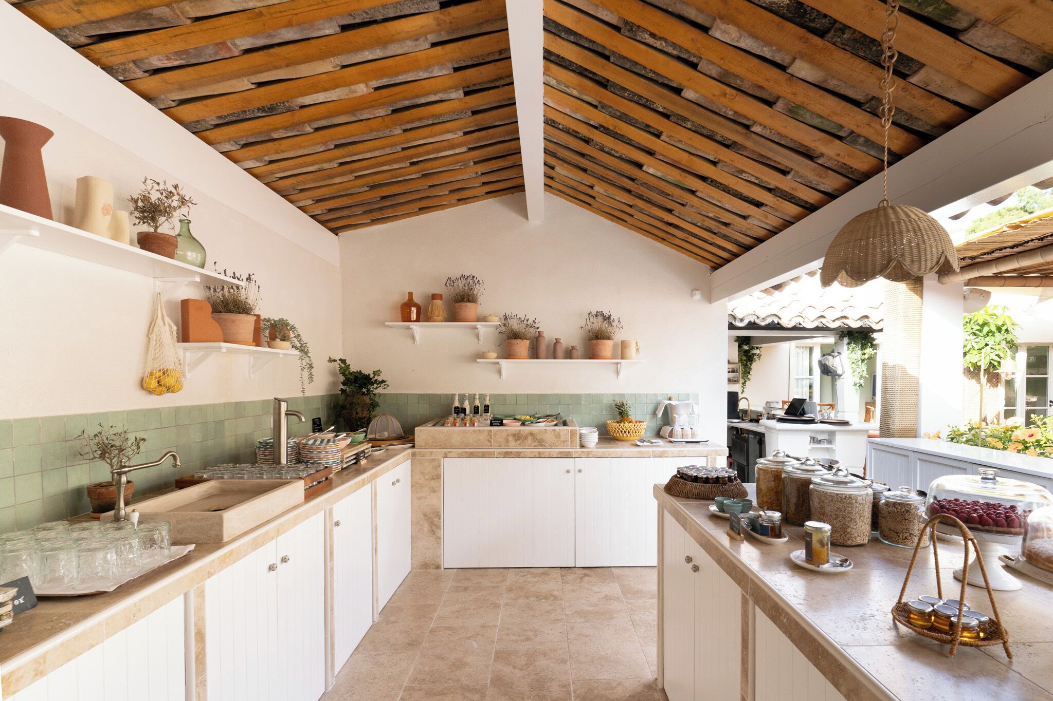 Una cocina con techo de madera rústica, armarios blancos y varios utensilios de cocina sobre las encimeras.