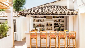 An outdoor bar area with a tiled roof, wooden chairs, and a variety of bottles.
