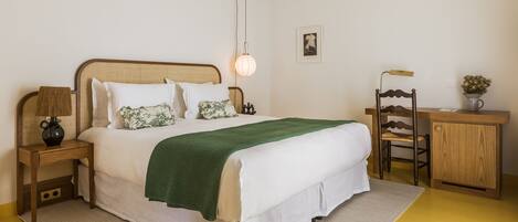 A neatly arranged bedroom with a bed, bedside tables, a desk, and a chair.