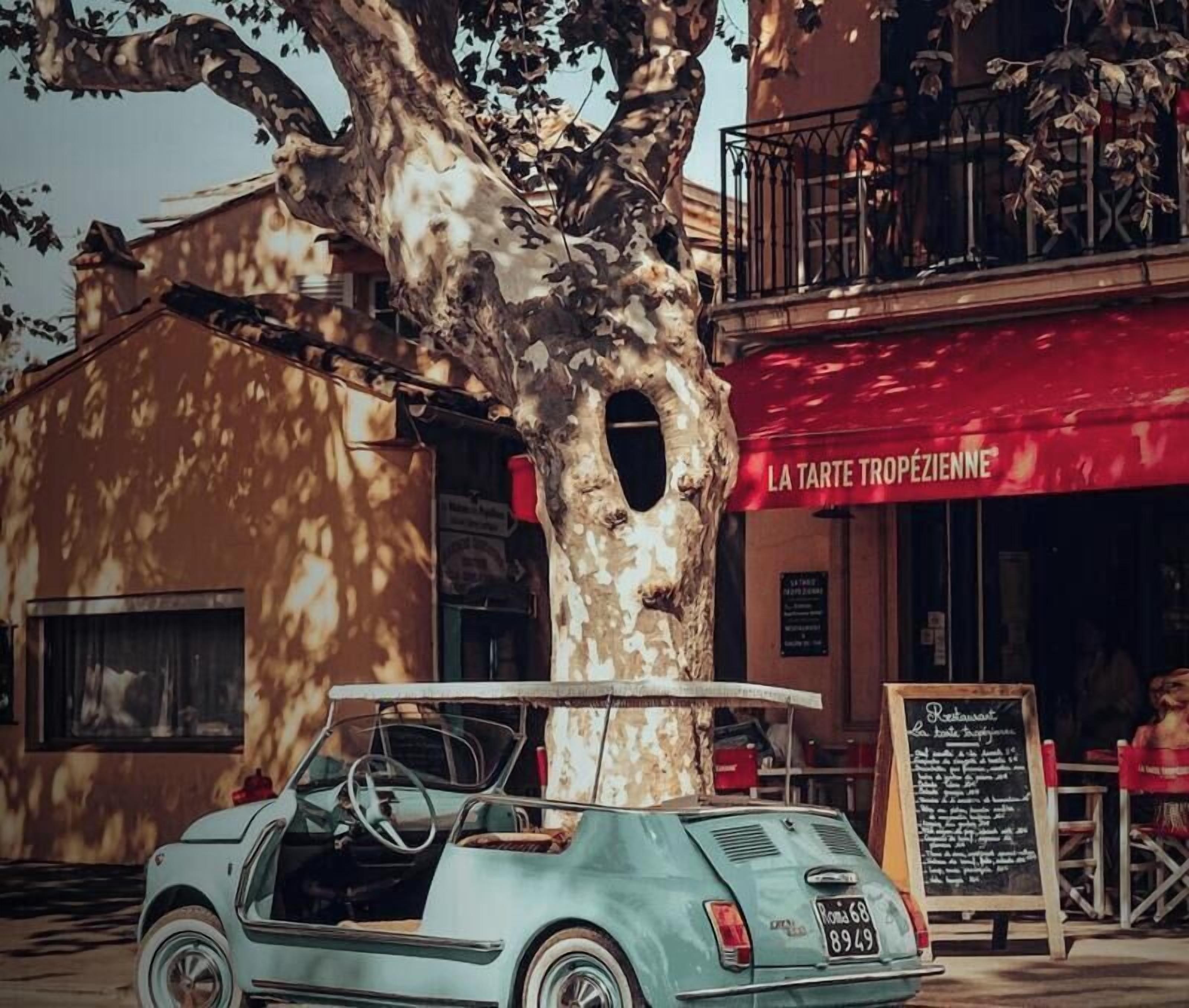 Un coche antiguo estacionado frente a un edificio con toldo rojo y un letrero que dice 'LA TARTE TROPÉZIENNE'.
