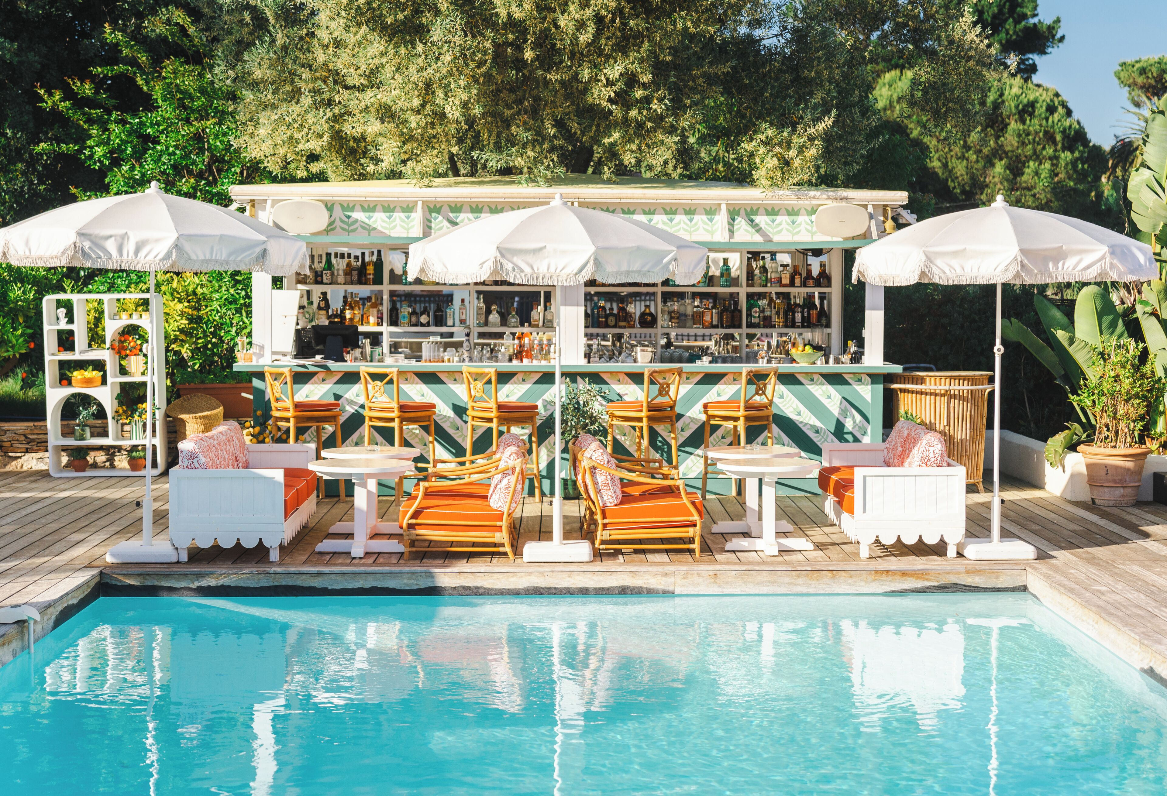 Un bar situé au bord de la piscine, doté d’une terrasse et de parasols, entouré d’une plateforme en bois et de verdure.