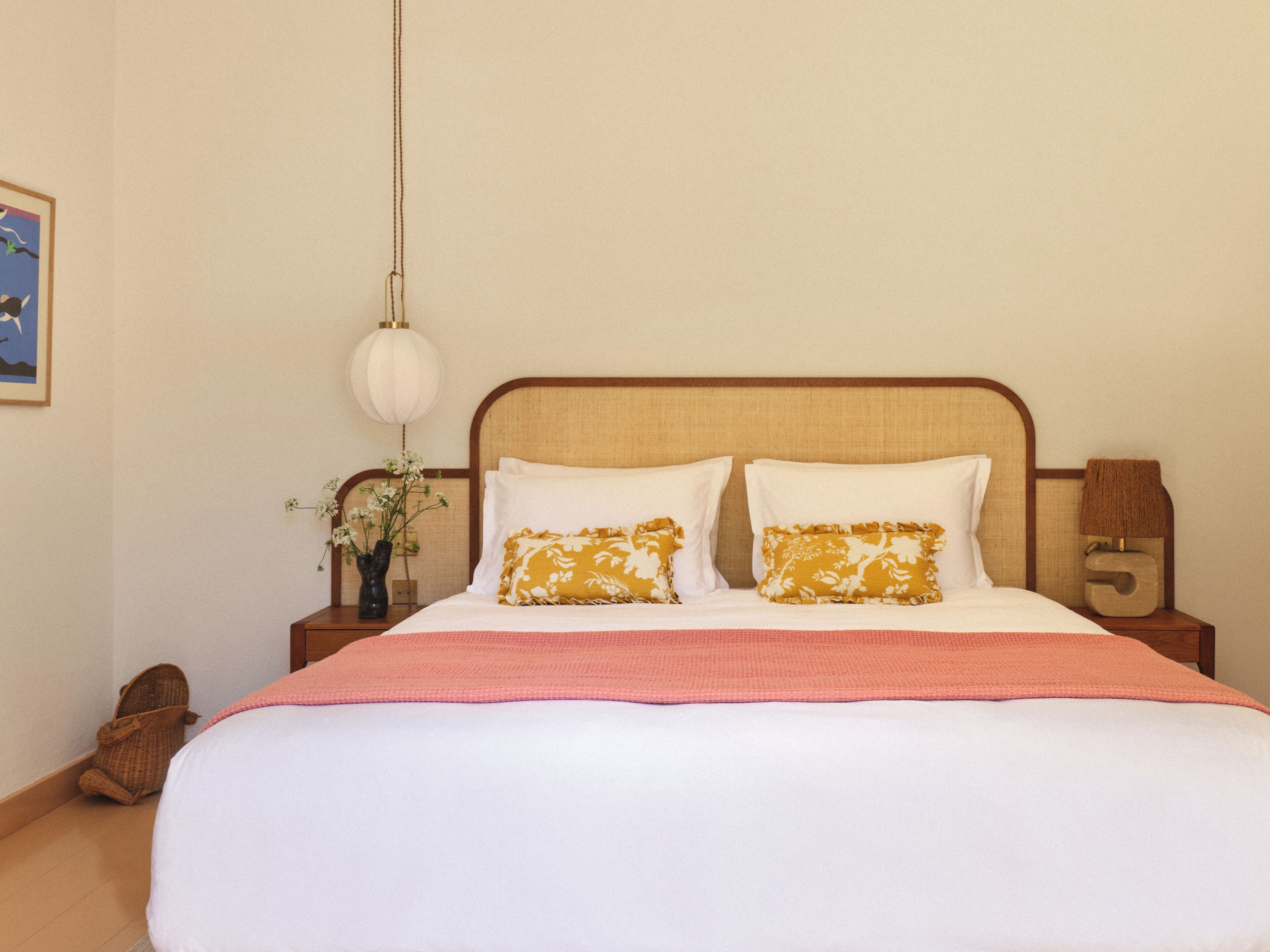 Een opgemaakt bed met witte en gele kussens, een roze deken en een houten hoofdbord.