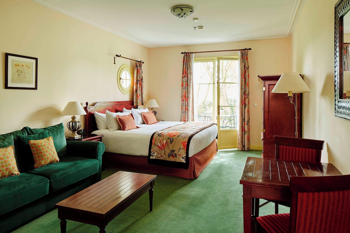 A hotel room with a bed, green sofa, wooden table, and a chair.