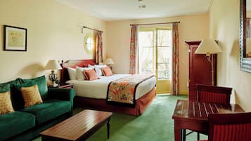 A hotel room with a bed, green sofa, wooden table, and a chair.
